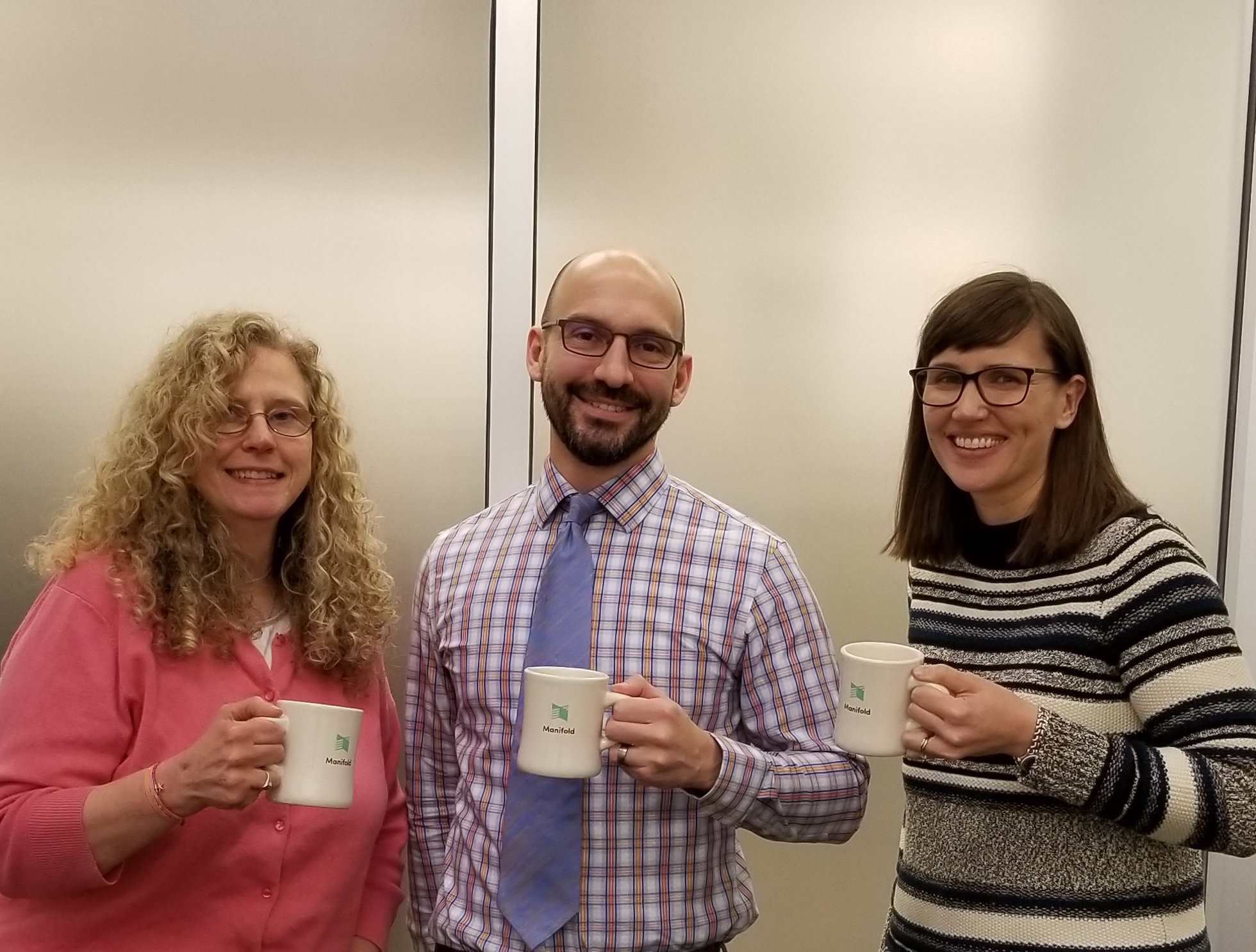 Group photo of Mary Rose Muccie, Terence Smyre, and Annie Johnson holding Manifold mugs, smiling