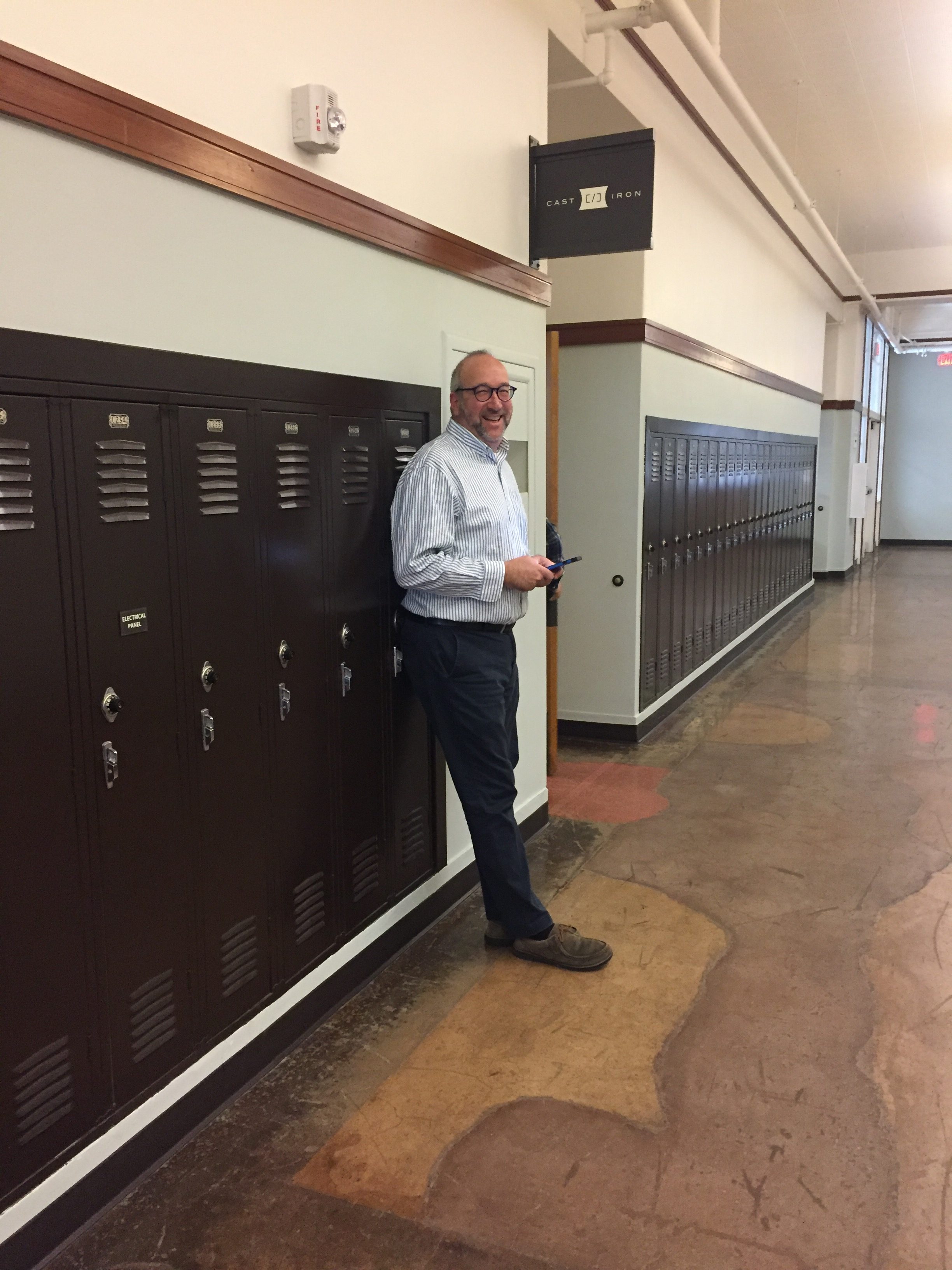 Doug in a school hallway with lockers under Cast Iron Coding sign